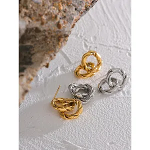 Elegant twisted hoop stud earrings in gold and silver finish on textured stone background