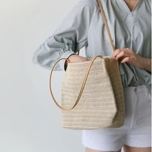 Lifestyle detail of a woven straw shoulder bag with long leather straps