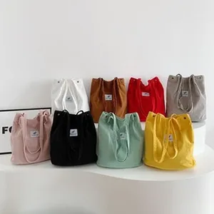 Various colorful corduroy tote bags in solid colors displayed on a white stand.