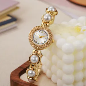 Détail d'une montre à quartz dorée de luxe avec un bracelet en perles blanches pour femme.