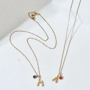 Macro view of gold initial M and A necklaces with blue and red birthstone charms