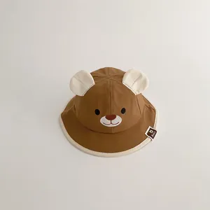 Close-up detail of a brown infant bucket hat featuring 3D bear ears and embroidered face.