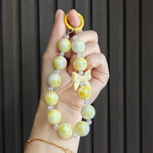Close-up detail of a candy-colored beaded phone charm featuring a yellow ring and bow