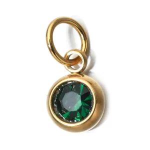 Detail view of a round gold stainless steel pendant with a faceted green gemstone.