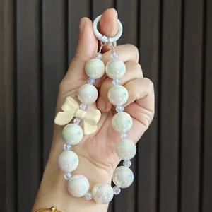 Detailed view of iridescent beaded keychain with a cream-colored resin bow charm