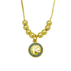 Detailed view of an 18K gold plated necklace with a "fé" pendant and blue beads.