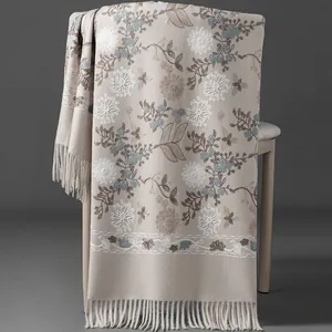 Elegant beige hand-embroidered floral scarf with tassels draped over a chair for winter warmth