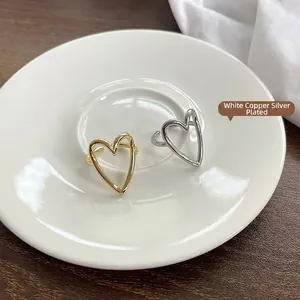 Minimalist heart-shaped open rings in gold and silver finishes on a white plate.