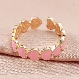 Primer plano detallado de anillo ajustable dorado con corazones de esmalte rosa en tela suave