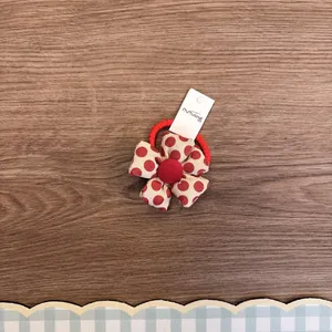 Nahaufnahme eines süßen Haargummis mit Stoffblume und roten Punkten auf Holztextur.