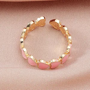 Primer plano macro de un anillo dorado ajustable con corazones de esmalte rosa.