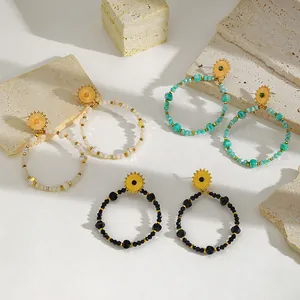 Close-up of three pairs of beaded hoop earrings with gold sunburst studs on stone.