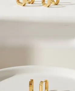 Nahaufnahme von minimalistischen goldenen rechteckigen Kreolen mit glänzend polierter Oberfläche