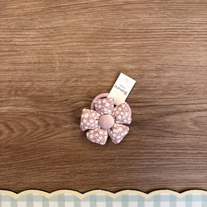 Detailansicht eines rosa geblümten Stoffblumen-Haargummis für Kinder auf Holzgrund
