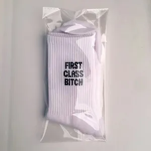 Detailed view of white cotton socks with First Class Bitch lettering in clear packaging