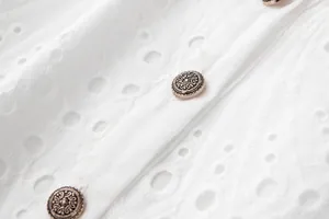 Gros plan sur la broderie anglaise blanche et les boutons dorés antiques de la robe