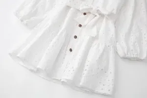 Gros plan de la robe chemise blanche à manches longues brodée avec boutons bronze et ceinture.