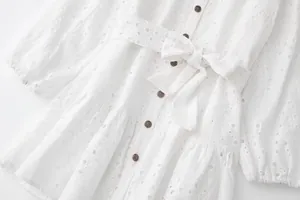 Vue détaillée d'une robe blanche en broderie anglaise avec boutons et nœud ceinture