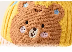 Nahaufnahme einer niedlichen Bärenstickerei auf einer gelb gestrickten Wintermütze für Kleinkinder