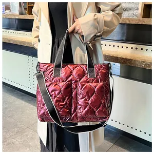 Wine red quilted puffer tote bag with wide shoulder strap carried by a model.