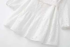 Gros plan sur le tissu brodé à œillets blancs d'une robe chemise à manches longues.