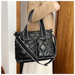 Large black quilted puffer tote bag with striped wide shoulder strap worn by a model