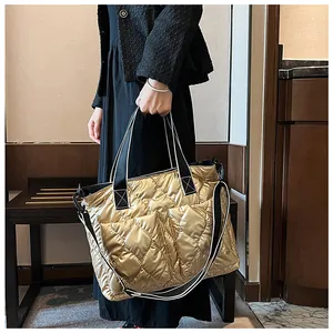 Detail view of a metallic gold quilted tote bag with a striped wide shoulder strap
