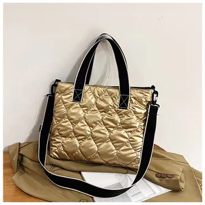 Golden quilted puffer tote bag with black and white wide strap styled on a brown coat