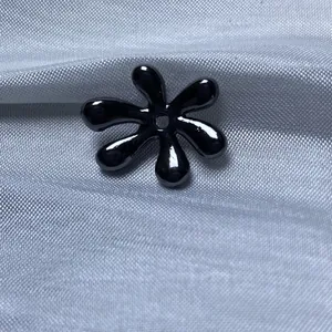 Vue macro d'une perle de bijoux DIY noire brillante en forme de fleur sur tissu texturé