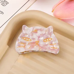 Close-up detail of a pink marbled acetate cat-shaped hair claw clip displayed on a beige tray.