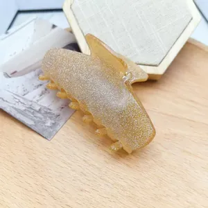 Close-up of a glittery golden cat-shaped hair claw clip on a light wooden background.