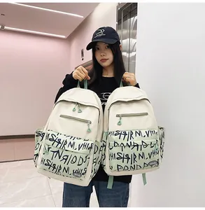 Asian model holding two large capacity student backpacks with graffiti print details