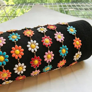 Gros plan de chaînes marguerites en émail coloré sur velours noir, acier inoxydable doré 18 carats.
