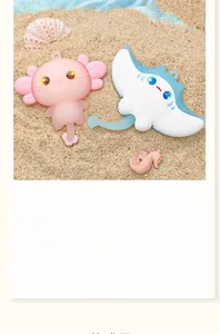A macro detail view of cute cartoon axolotl and manta ray bag charms resting on sea sand.