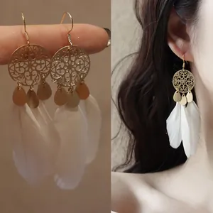 Close-up detail of bohemian white feather long hook earrings with gold hollow patterns.