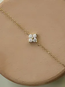 Close-up of gold-plated clover anklet with four sparkling crystals on wooden display