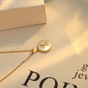 Gros plan d'un collier doré avec pendentif rond en nacre et gravure de la lettre X.