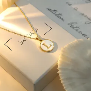 Gros plan d'un collier doré avec un pendentif circulaire en nacre et la lettre L.
