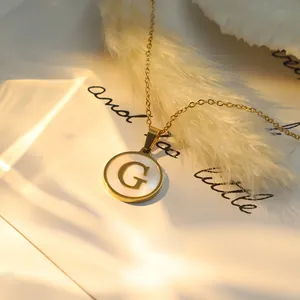 Vue détaillée d'un collier doré avec un pendentif en nacre orné de la lettre G initiale.
