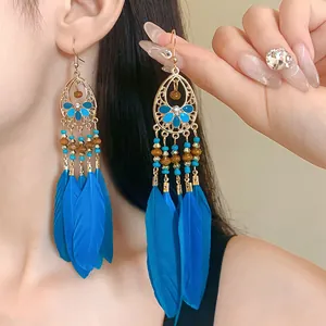 Detailed close-up of long bohemian blue feather earrings with intricate gold beads