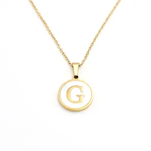 Détail en gros plan du collier avec pendentif rond en nacre dorée et la lettre G