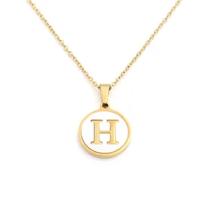 Détail d'un collier rond en or avec un pendentif en nacre blanche avec la lettre H