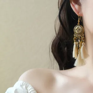 Detailed view of Bohemian long drop earrings with cream tassels and gold feather charms