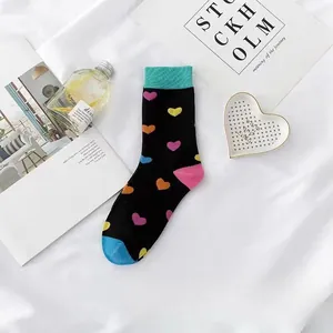 Detail von schwarzen Crew-Socken mit bunten Herzmustern und blaugrünen Bündchen.