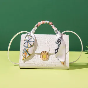 Detail view of a white crocodile pattern handbag with a silk scarf wrapped handle.