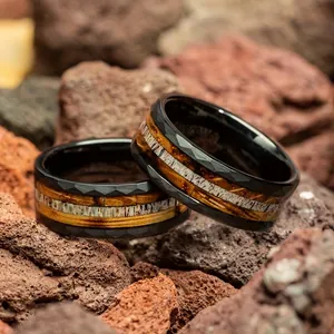 Close-up of faceted black stainless steel rings with wood and bone inlay on volcanic rocks