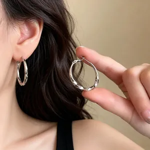 Detail shot of silver twisted metal hoop earrings showing polished texture and wear effect.