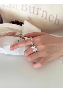 Vista detallada de anillo abierto de plata S925 con lazo blanco y piedras rosa corazón.