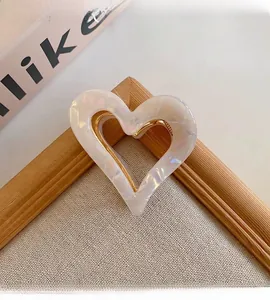 Close-up detail of a pearly white heart-shaped hair claw clip with elegant gold finish