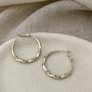 Detailed view of gold-plated twisted hoop earrings on a speckled ceramic plate